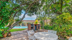 Um pátio com mesa e cadeiras redondas, lareira de tijolos e piscina ao fundo.