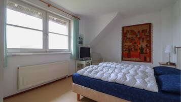 A bedroom with a bed, a television, a chair, a radiator, and a window with curtains.
