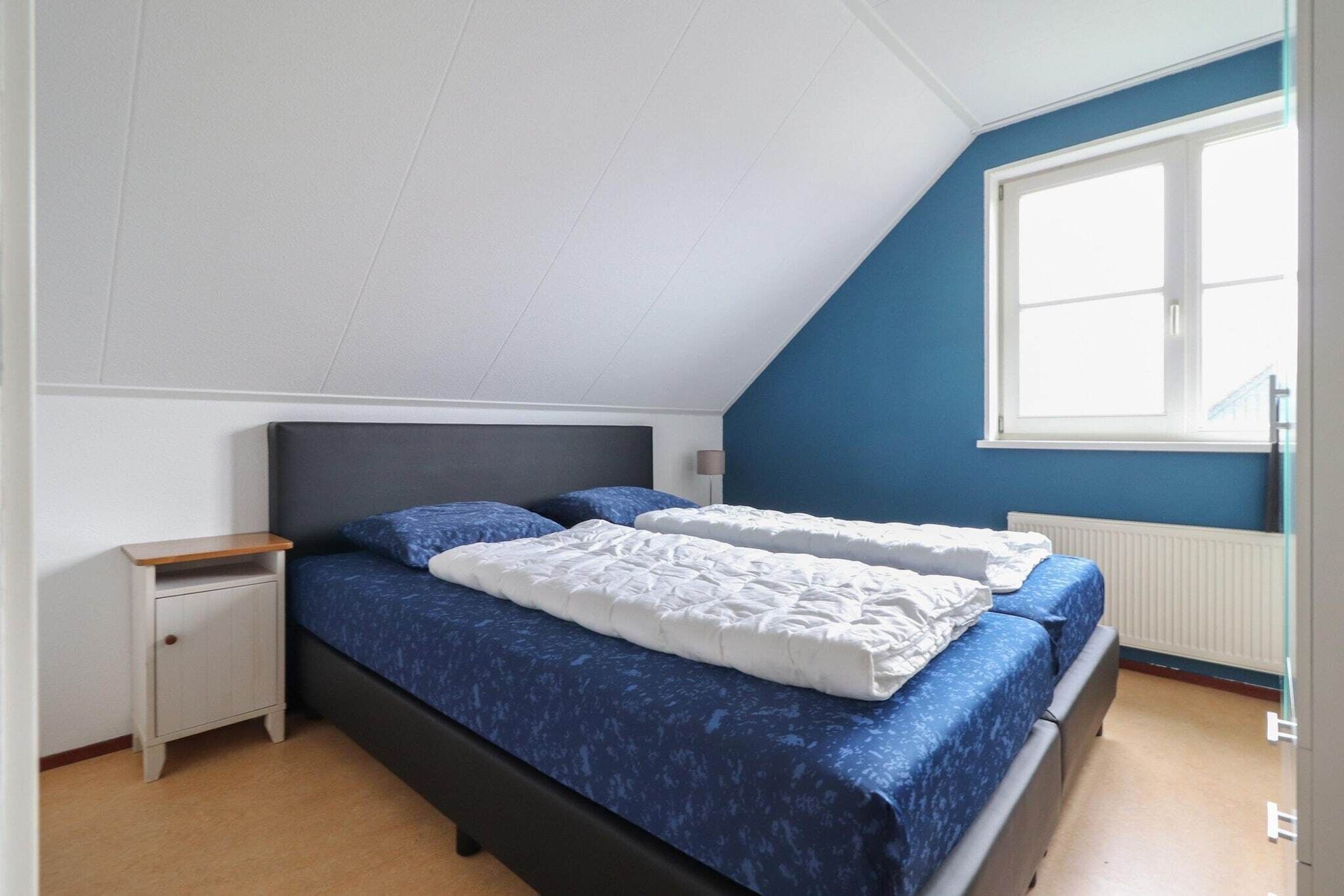 A bedroom with a bed, a nightstand, a window, and a radiator.