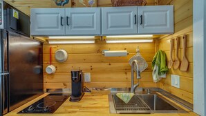 Une cuisine avec des meubles en bois, un réfrigérateur en acier inoxydable, une machine à café, un évier et des ustensiles de cuisine en bois accrochés au mur.