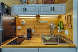 A kitchen with wooden cabinets, a stainless steel refrigerator, a coffee maker, a sink, and wooden utensils hanging on the wall.