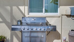 En grill i rustfrit stål med kontrolpanel og indbygget ovn, placeret op ad en struktureret væg med et vindue over.