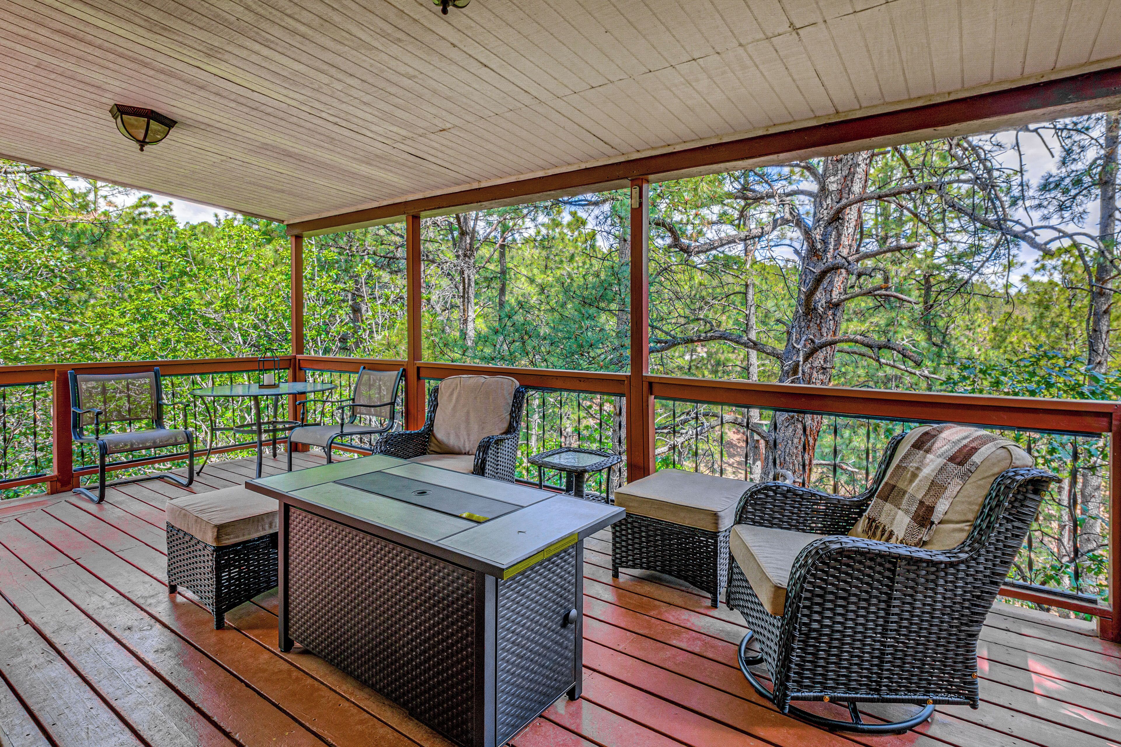 A covered outdoor area with a table and chairs, surrounded by trees.