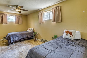 Een slaapkamer met twee bedden, een plafondventilator en ramen voorzien van gordijnen.