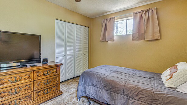 A bedroom with a bed, dresser, television, and a closet with sliding doors.