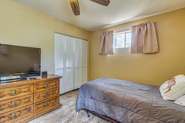 A bedroom with a bed, dresser, television, and a closet with sliding doors.
