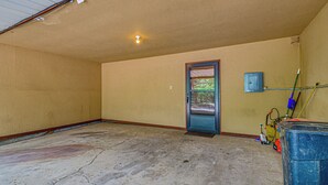 A room with a concrete floor, a door with a view of greenery, a blue utility box, and a mop on the right.