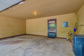 A room with a concrete floor, a door with a view of greenery, a blue utility box, and a mop on the right.