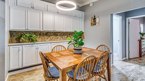 A kitchen with white cabinets, a wooden dining table with chairs, and a hanging light fixture.