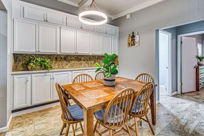A kitchen with white cabinets, a wooden dining table with chairs, and a hanging light fixture.