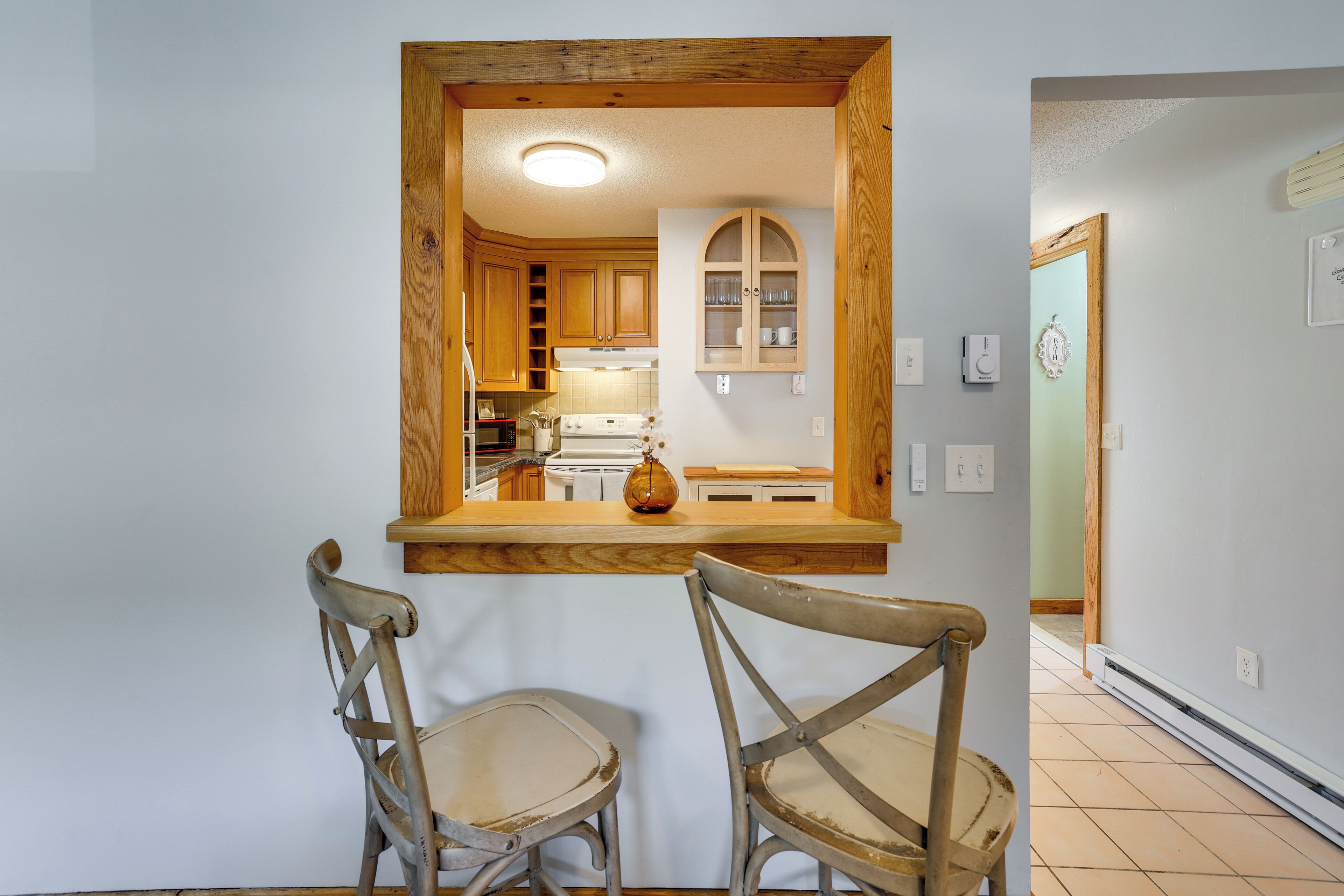 Une cuisine avec des meubles de rangement en bois, un four encastré et un coin repas avec deux chaises.
