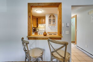 A kitchen with wooden cabinets, a built-in oven, and a dining area with two chairs. - Bristol Condo Near ESPN HQ & Lake Compounce! (Bristol)