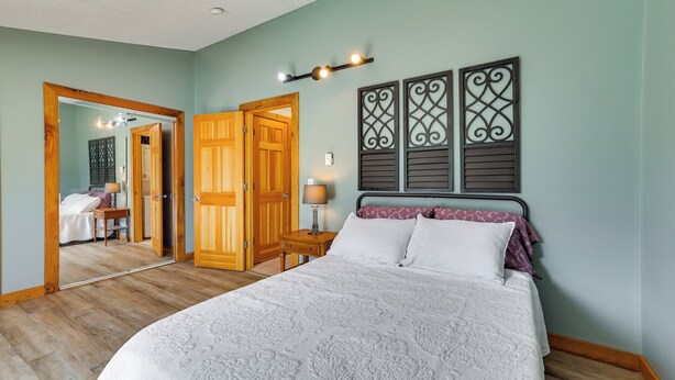 Ein Schlafzimmer mit einem großen Bett, einer Holztür, einem Spiegel und einer Wandleuchte.