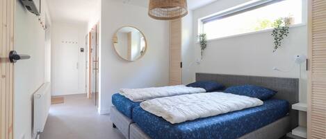 Une chambre avec un grand lit, un luminaire suspendu, une fenêtre ornée de plantes et un miroir au mur.