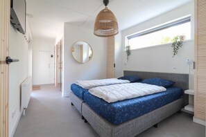Ein Schlafzimmer mit einem Bett, einer Hängeleuchte, einem Fenster mit Pflanzen und einem Spiegel an der Wand.