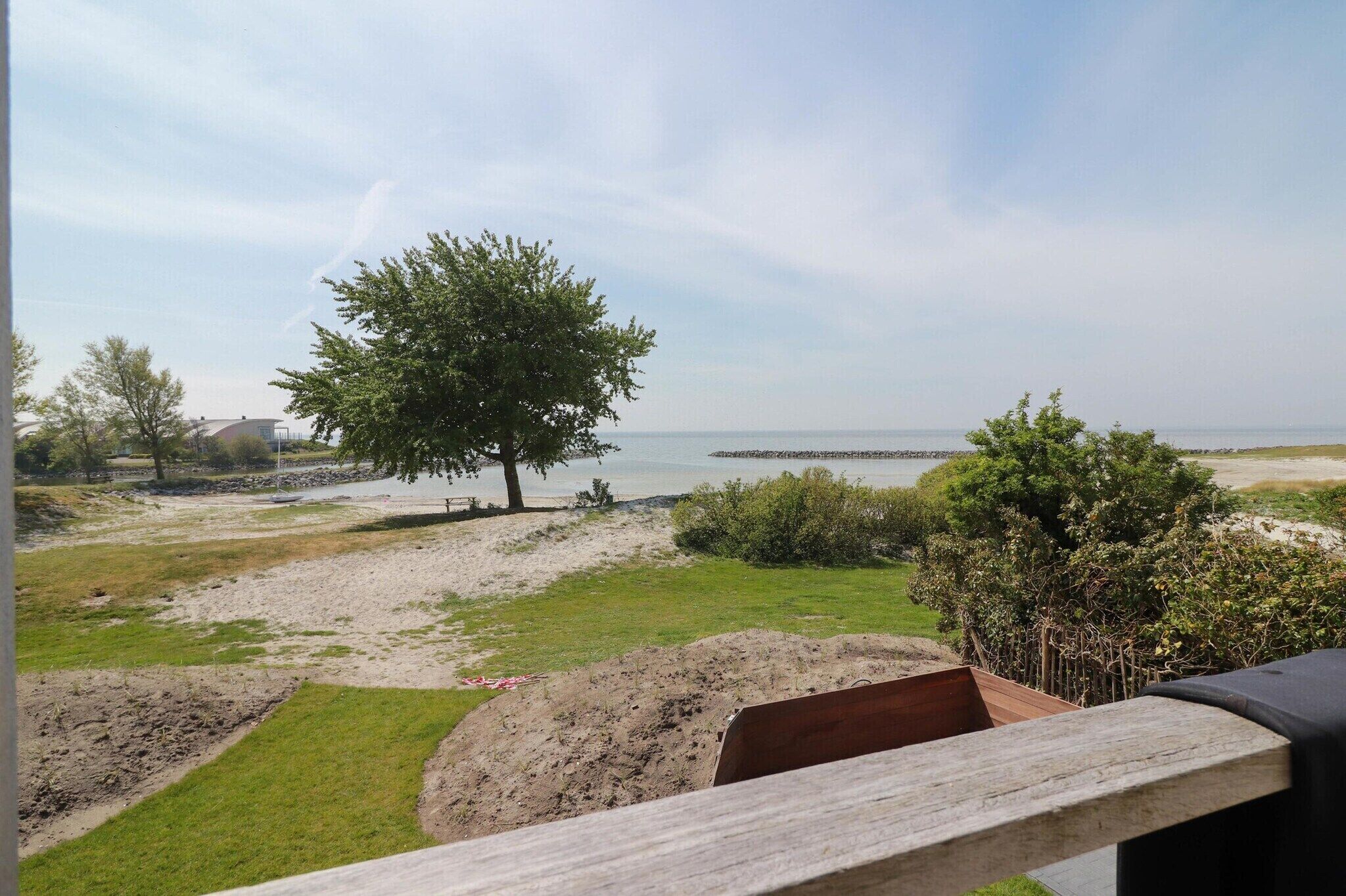 Une vue sur une plage avec une terrasse en bois, un arbre et une jetée au loin.