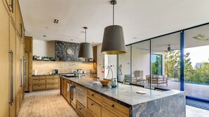 A modern kitchen with wooden cabinets, a marble island, pendant lighting, and a view of the outdoors. - 6,000-Sq-Ft Hollywood Hills Home w/ Pool, Hot Tub (Los Angeles)