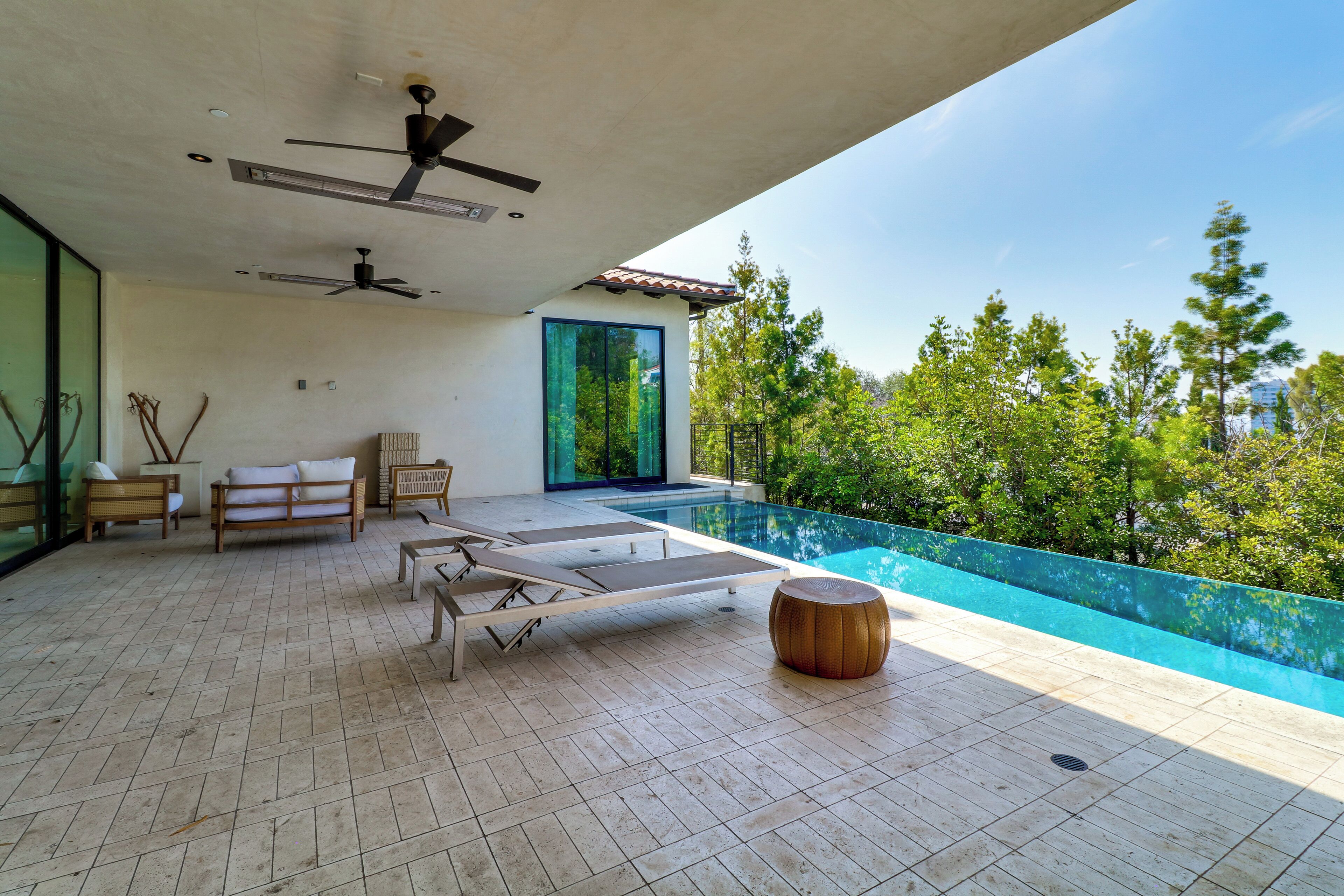 Un área de lounge exterior moderna con piscina, asientos y un ventilador de techo.
