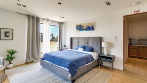 A modern bedroom with a large bed, a nightstand, a lamp, and a view of the outdoors. - 6,000-Sq-Ft Hollywood Hills Home w/ Pool, Hot Tub (Los Angeles)