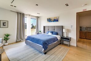 Ein modernes Schlafzimmer mit einem großen Bett, einem Nachttisch, einer Lampe und Blick ins Freie.