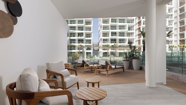 Un espace de détente moderne, doté de meubles en bois, offrant une vue sur la piscine et agrémenté d’une balustrade en verre.