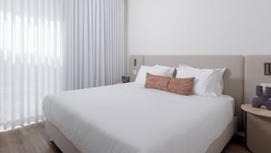 Une chambre d’hôtel avec un grand lit, du linge de lit blanc, un coussin décoratif à motifs et une table de chevet avec une lampe.