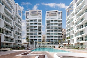 Un hotel moderno con piscina central, varios balcones y cielo despejado.