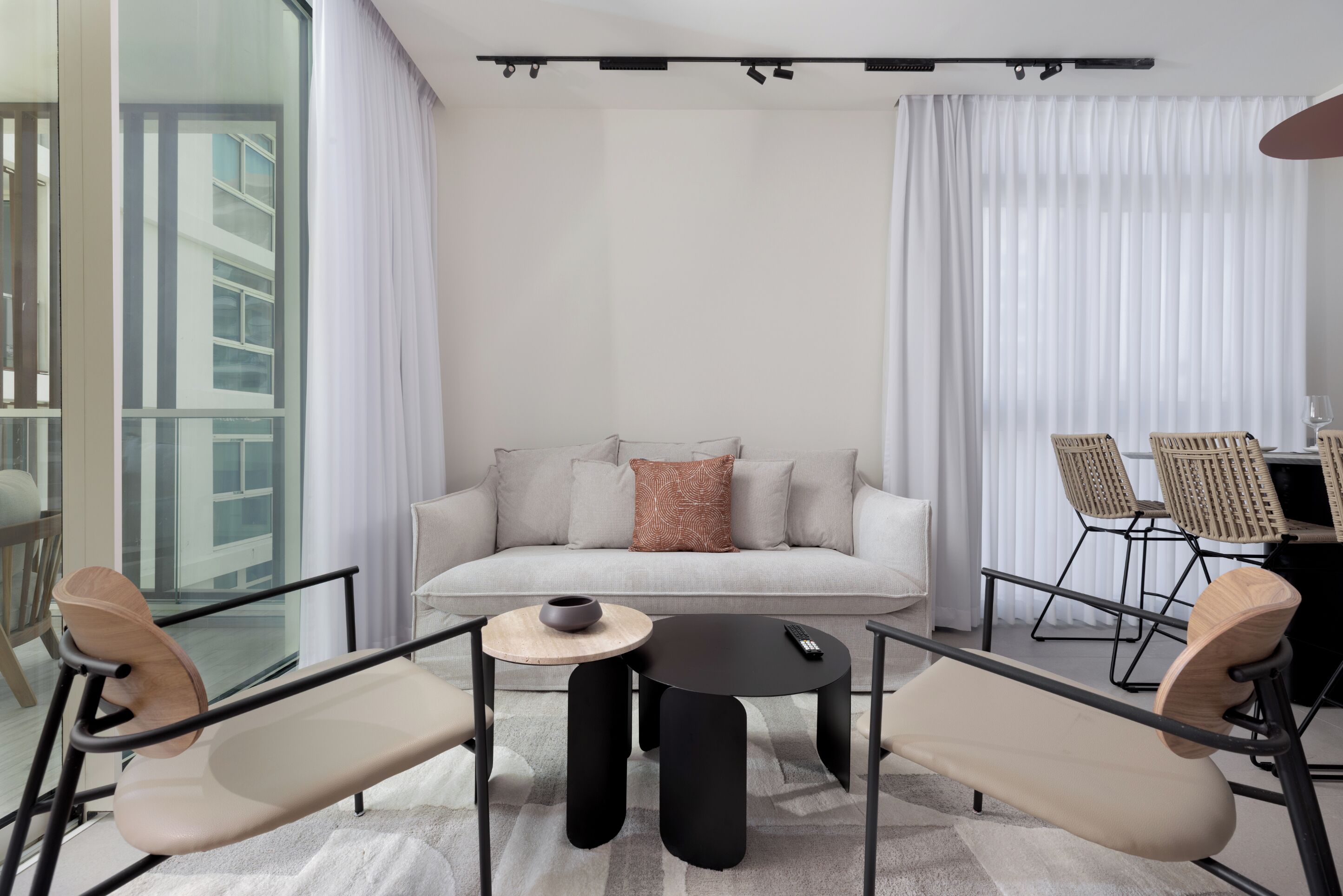 Uma sala de estar moderna com um sofá, duas poltronas, uma mesa de centro e uma área de jantar com cadeiras.