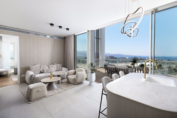A modern living room with a large window, a sofa set, a coffee table, and a bar area with a sink. - 42 Residence by Brown (Eilat)