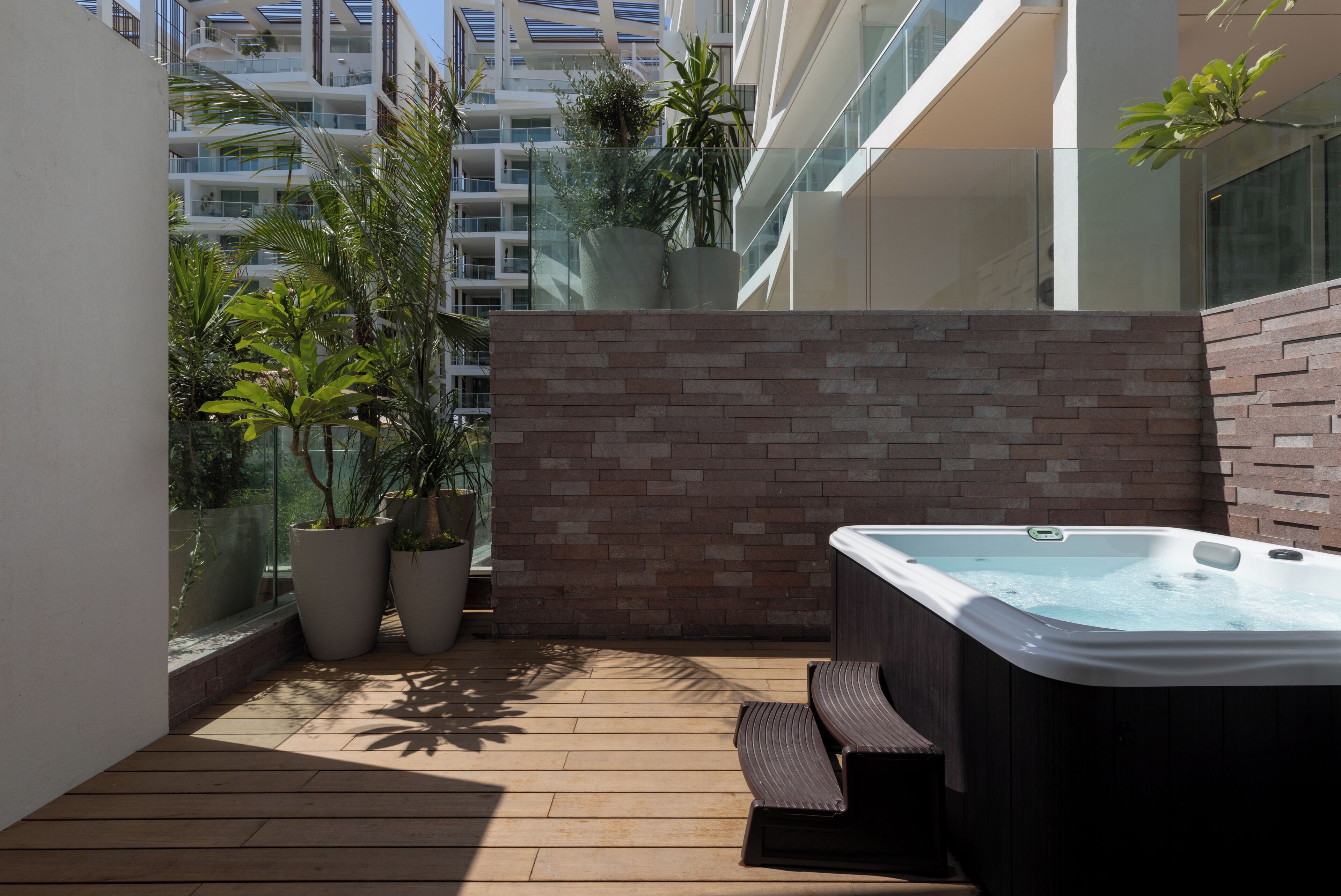 Un espacio exterior moderno con jacuzzi, plantas en macetas y una pared de ladrillo.