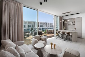 Una sala de estar moderna con un conjunto de sofá, una mesa redonda de centro y un área de comedor con taburetes de bar.