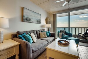A modern living room with a sofa, a coffee table, a lamp, a painting, and a balcony with a view. - Unwind Poolside, Walk to Shore! Ponce Inlet Escape (Ponce Inlet)
