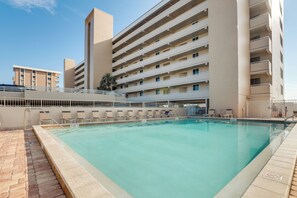 A swimming pool with a brick border, a white fence, and a building with multiple balconies in the background. - Unwind Poolside, Walk to Shore! Ponce Inlet Escape (Ponce Inlet)