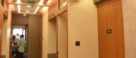 Un couloir d’hôtel avec un comptoir de réception, des portes en bois et un plafond doté d’un éclairage encastré.