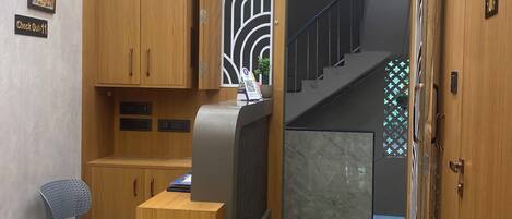 A hotel lobby with a reception desk, a seating area, a staircase, and a decorative wall.
