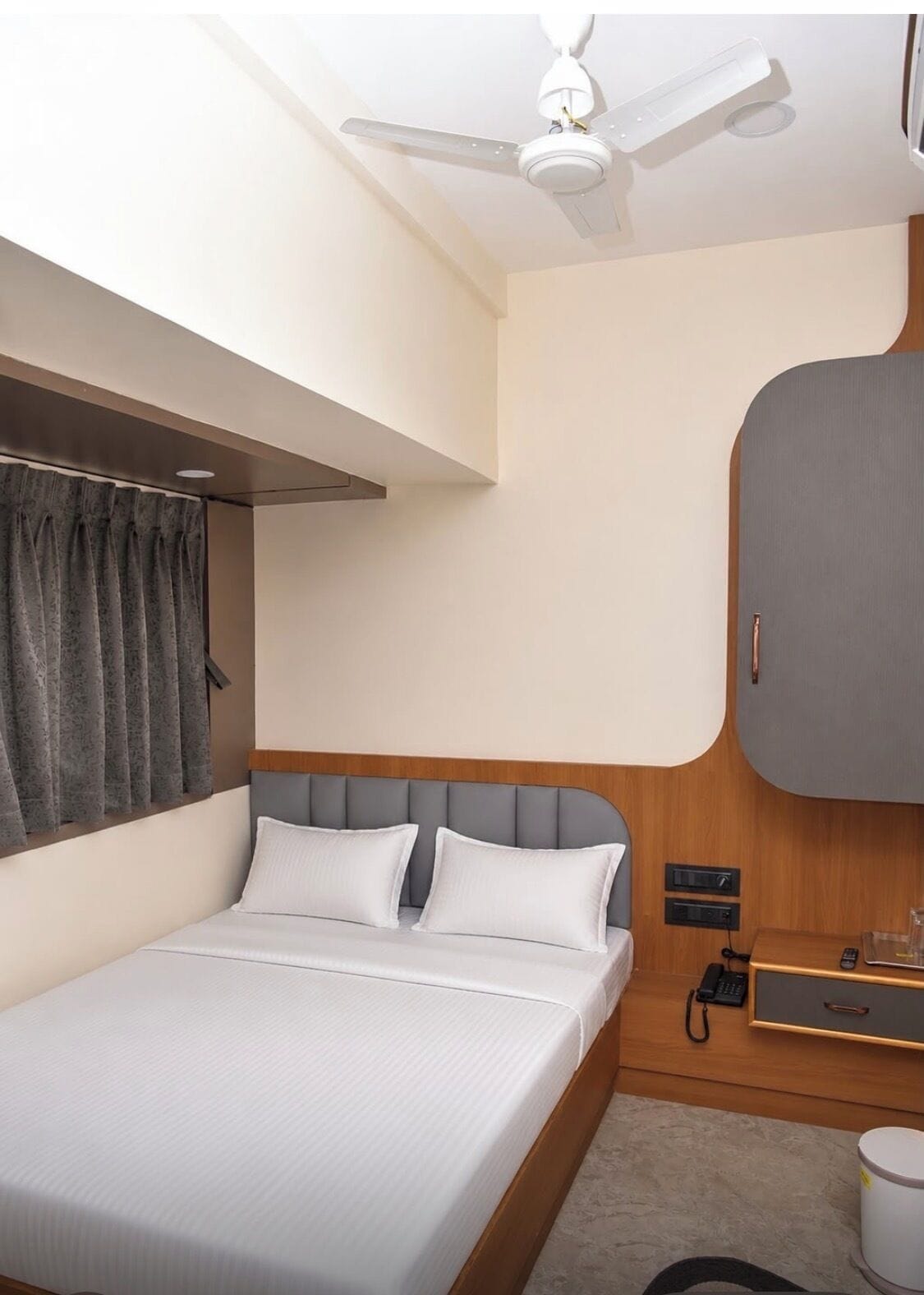 Una habitación de hotel con una cama, un ventilador de techo, un armario y una mesita de noche con un teléfono.