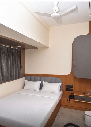 Quarto de hotel com cama, ventoinha no teto, guarda-roupa e mesa de cabeceira com telefone.