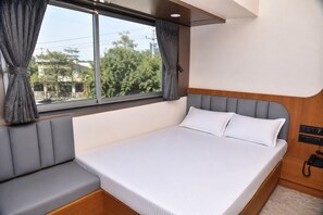 A bed with a headboard, a window with curtains, and a bedside telephone.