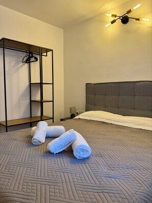 A hotel room with a bed, a hanging wardrobe, and a wall-mounted light fixture. - Apartment 39 sq.m. | Near Athens Airport & Beach (Αρτέμιδα)