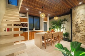 A modern kitchen with a central island, wooden staircase, and a stone wall. - 1 BR Beachside Retreat Blacksand Villas Bingin (Badung)