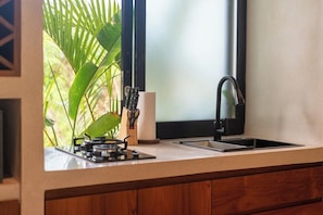 A kitchen with a gas stove, a sink, and a window with a view of greenery. - 1 BR Beachside Retreat Blacksand Villas Bingin (Badung)