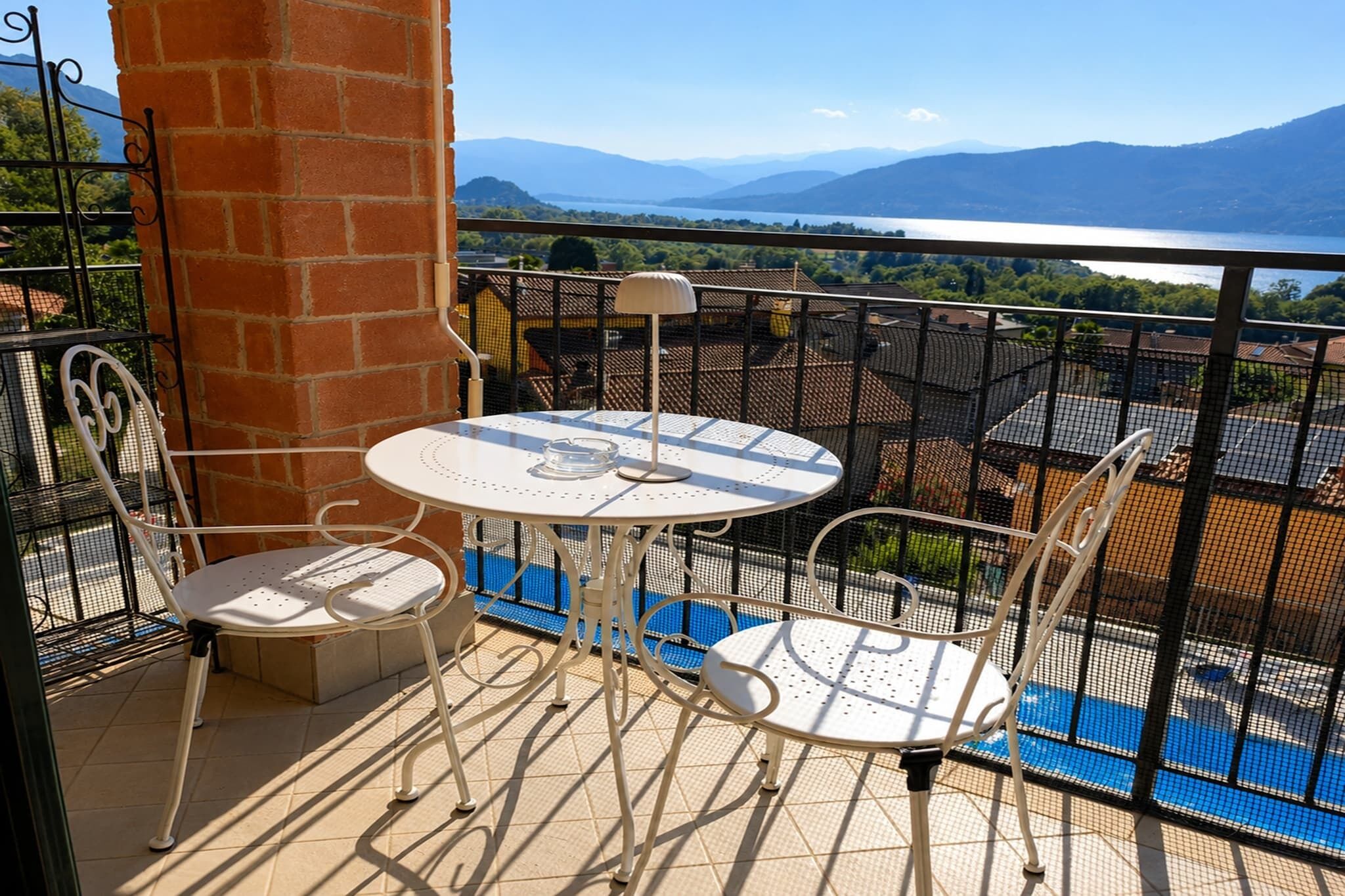Un balcón con mesa y sillas, vista a un lago y montañas, y un pilar de ladrillo.