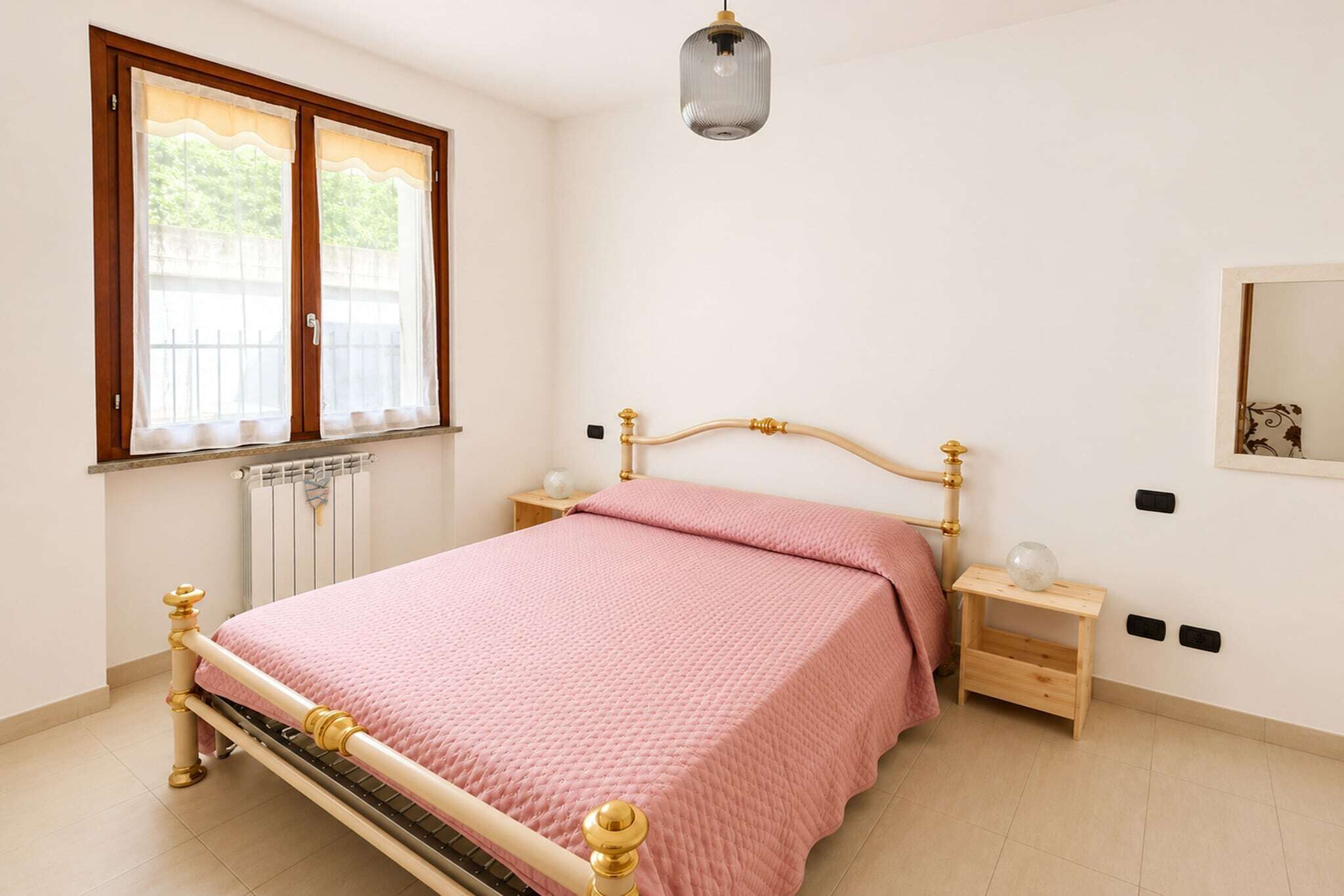 Ein Schlafzimmer mit einem Bett, einem Nachttisch, Vorhängen, einer Heizung und einer Pendelleuchte.