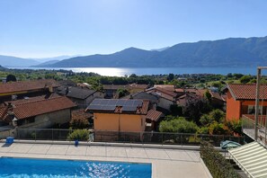 A residential area with a swimming pool, houses with red-tiled roofs, and a lake with mountains in the background.