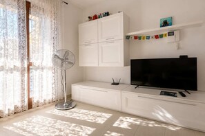 A modern living room with a flat-screen TV, a standing fan, and a cabinet.