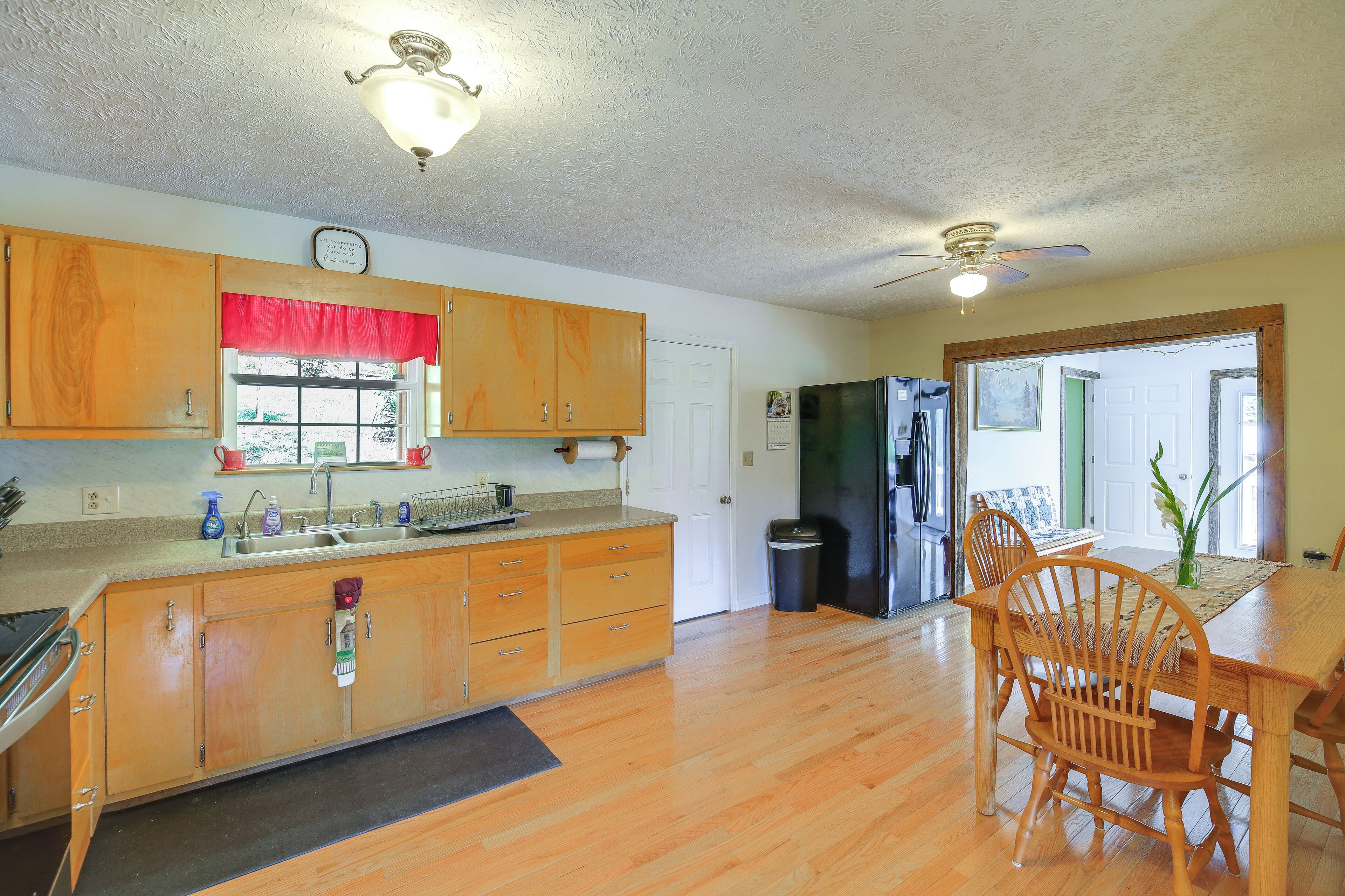 A kitchen with wooden cabinets, a refrigerator, a dining table with chairs, and a ceiling fan.