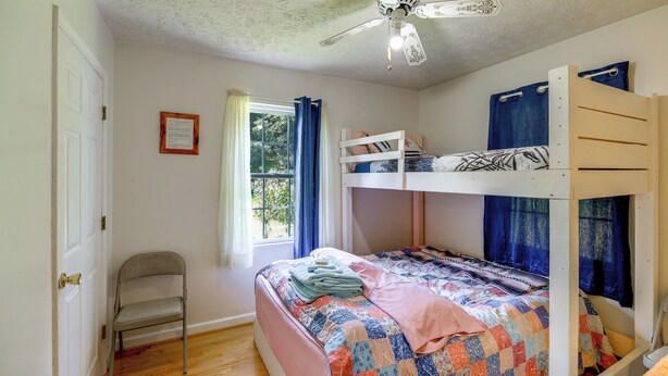 Ein Schlafzimmer mit Etagenbett, einem Einzelbett, einem Stuhl, einem Deckenventilator und einem Fenster mit Vorhängen.