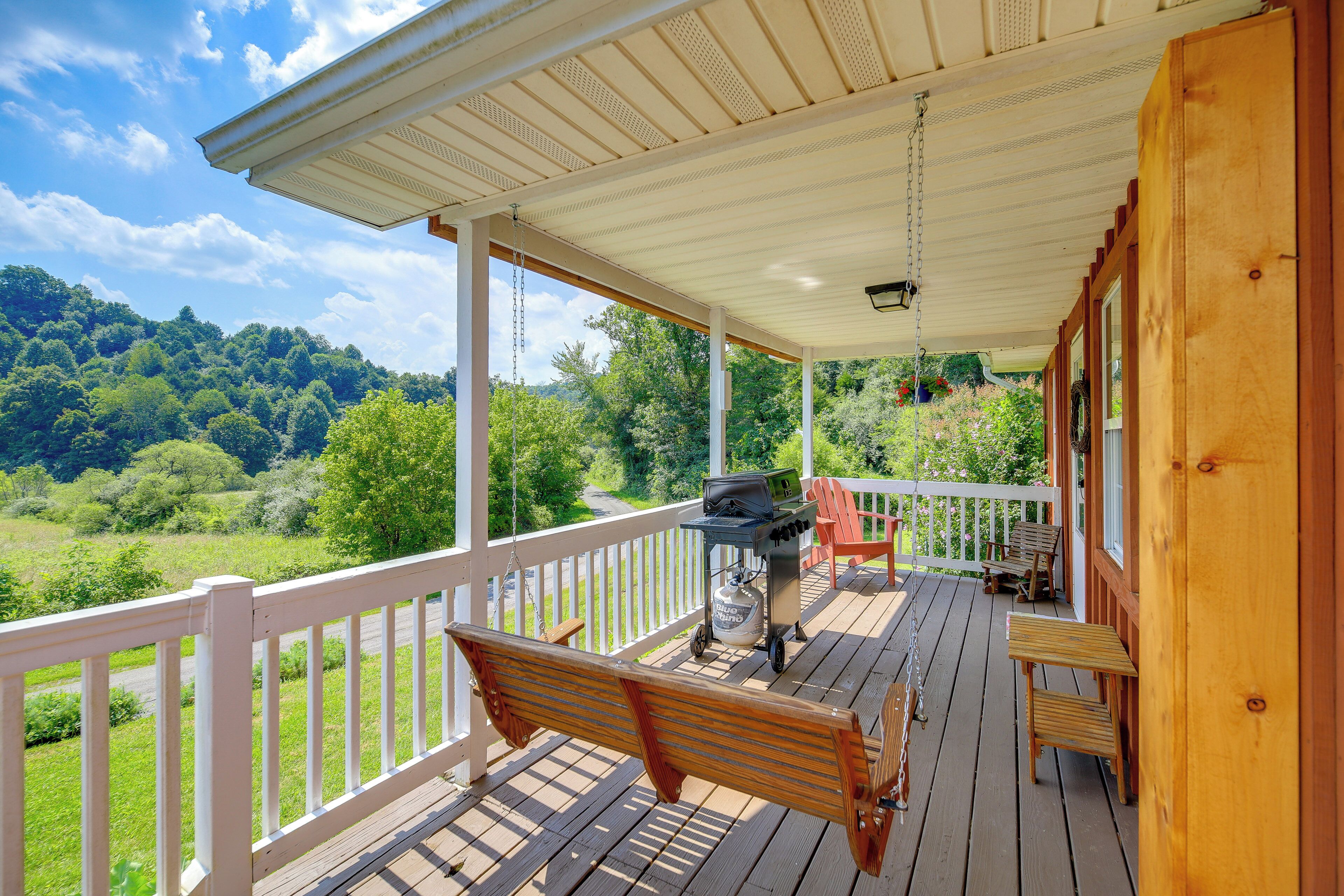 A wooden deck with a bench, a grill, and a view of a green landscape.