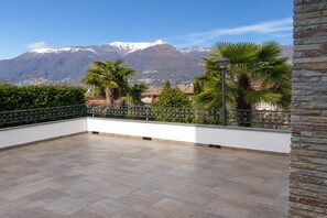 A terrace with a view of mountains, a stone wall, and a metal fence. - Lakeside Apartment in Germignaga for 4 (Germignaga)