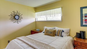 A bedroom with a bed, a bedside table, a clock, a window with curtains, and a wall-mounted artwork. - Bayfront Escape Near Boat Launch in Austwell (Austwell)
